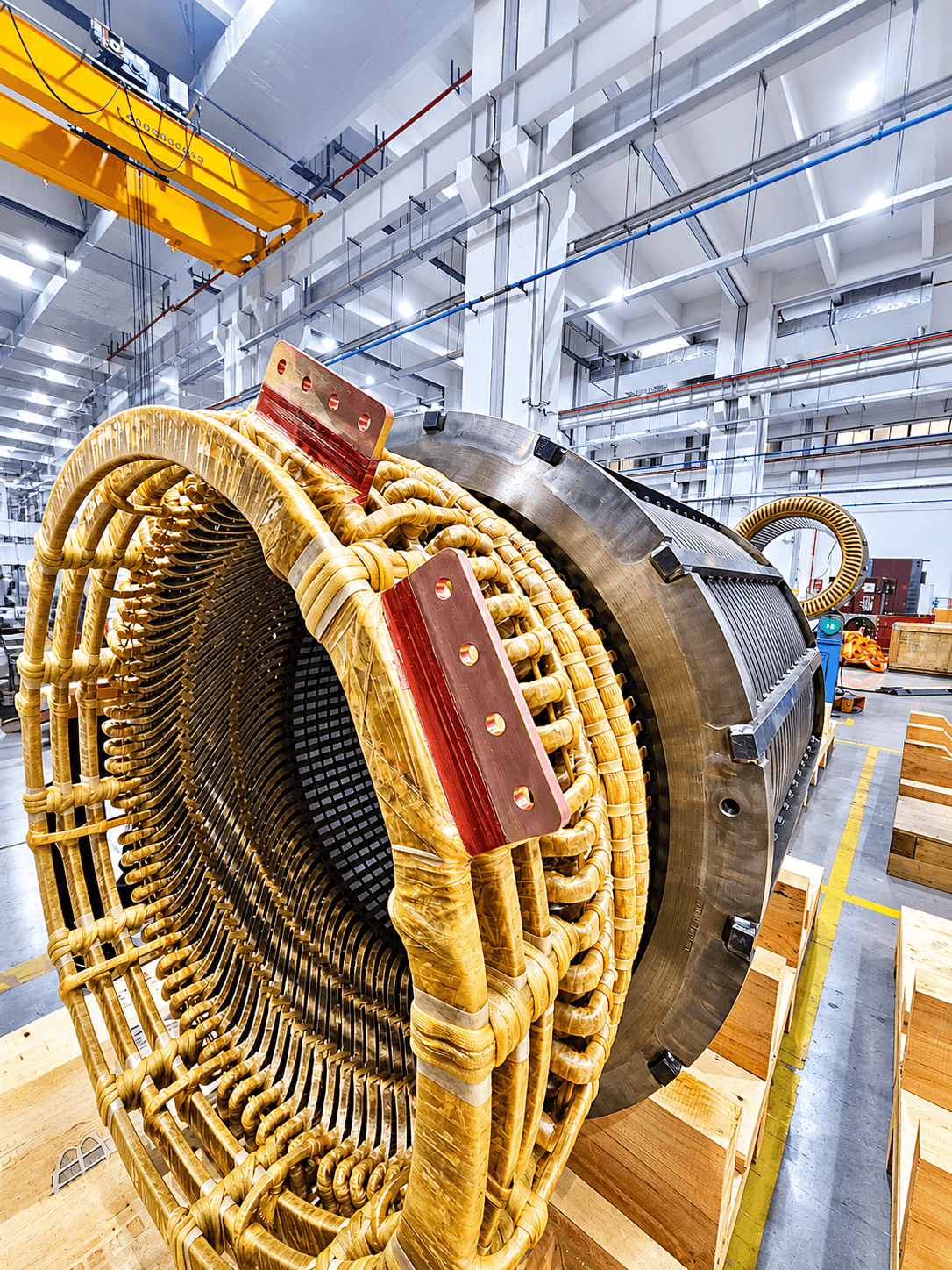 Large industrial stator with intricate yellow insulated copper windings inside a spacious factory workshop.