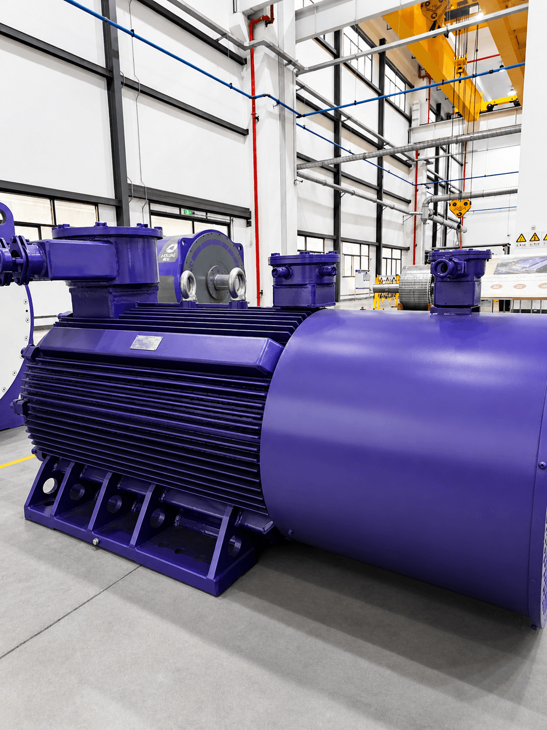 Large purple industrial motor with cooling fins and cylindrical housing on a factory floor.
