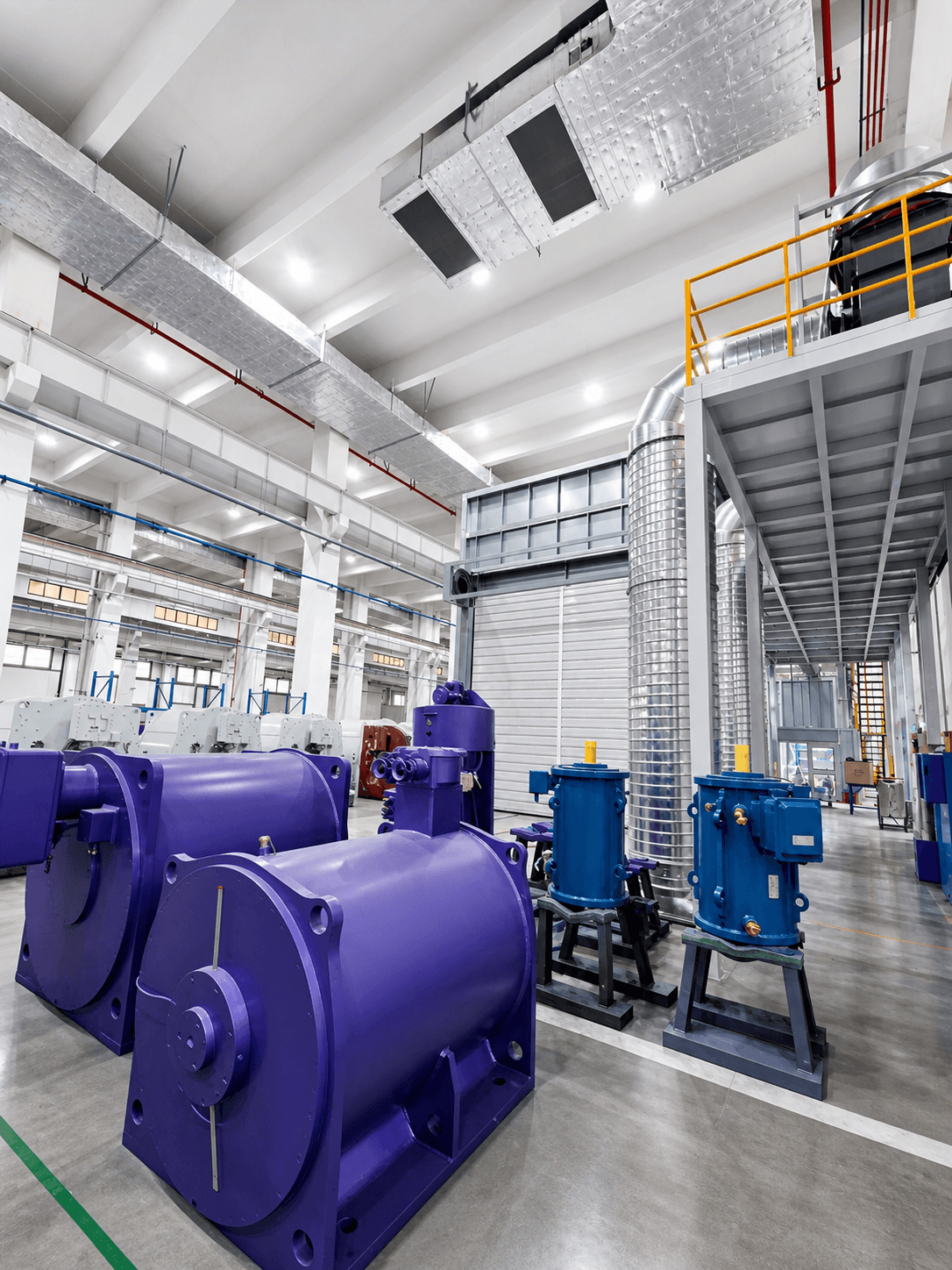Industrial facility with large purple and blue machines, silver ductwork, and high white ceilings.
